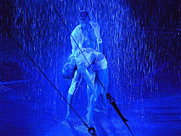 Mann und Frau in weißer, zerrissener Kleidung machen Akrobatik. Blaues Licht. Wasser von oben.